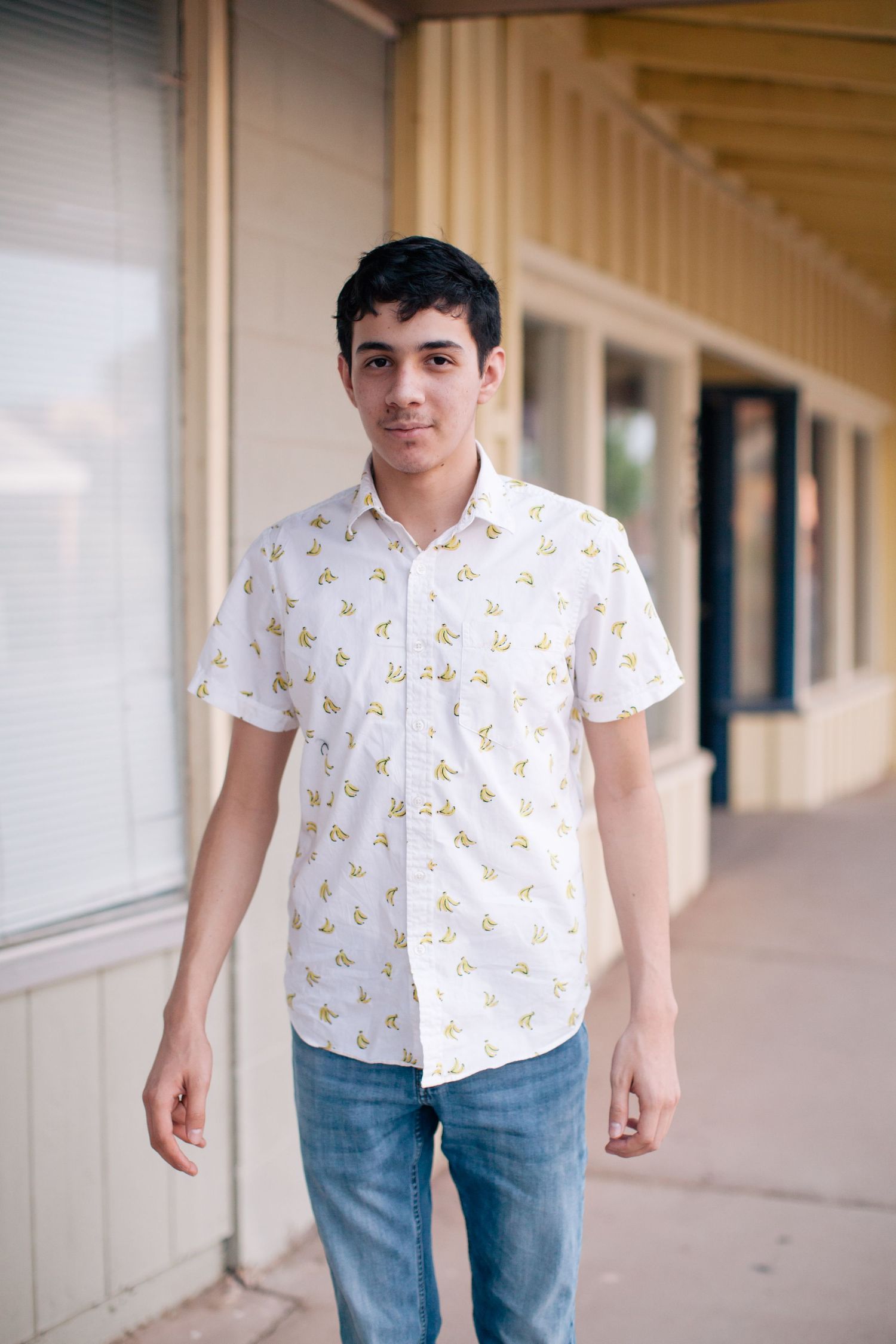 Standing portrait in front of storefront wearing white patterned button-up shirt.