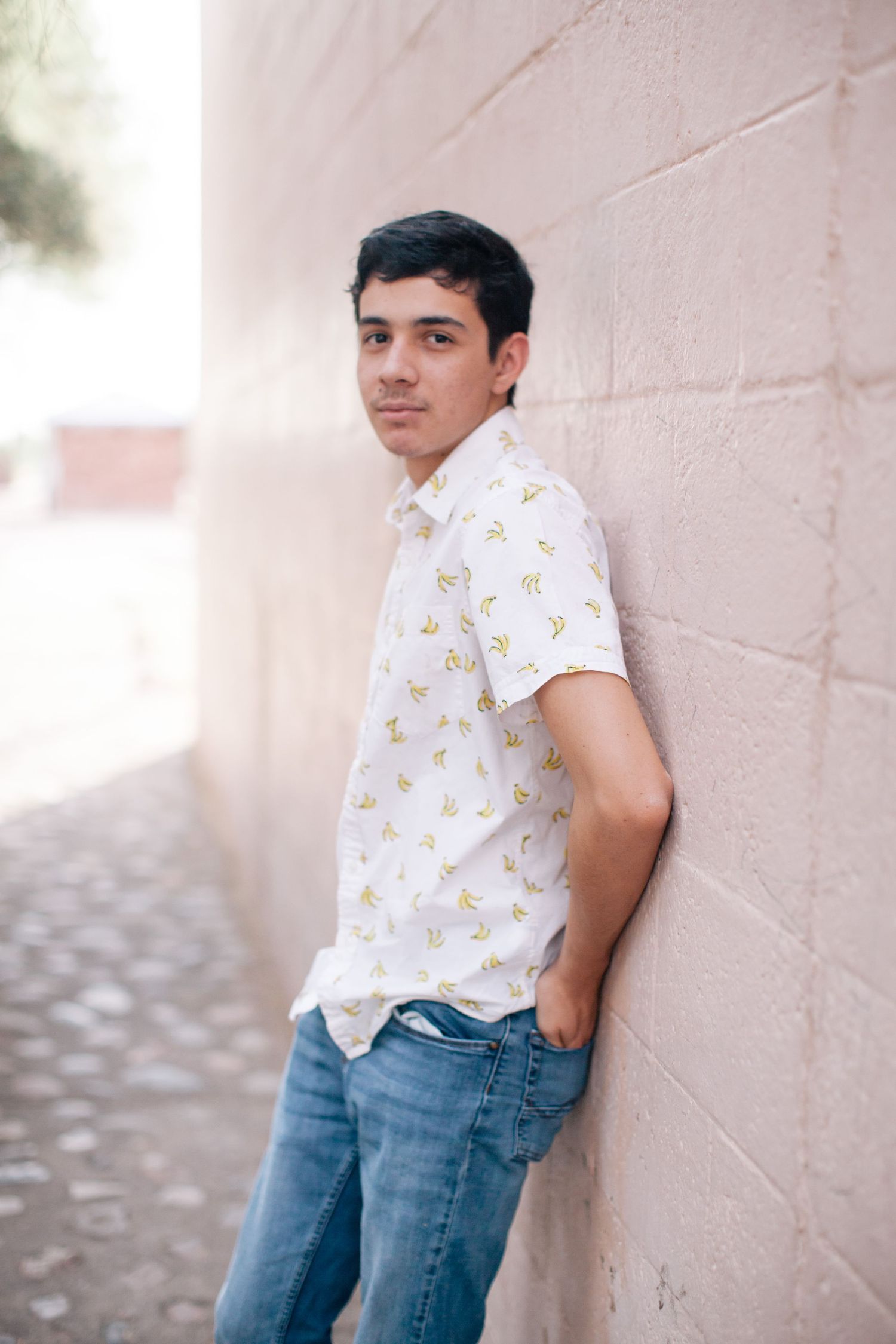Casual lean against pink wall in white patterned shirt and blue jeans.