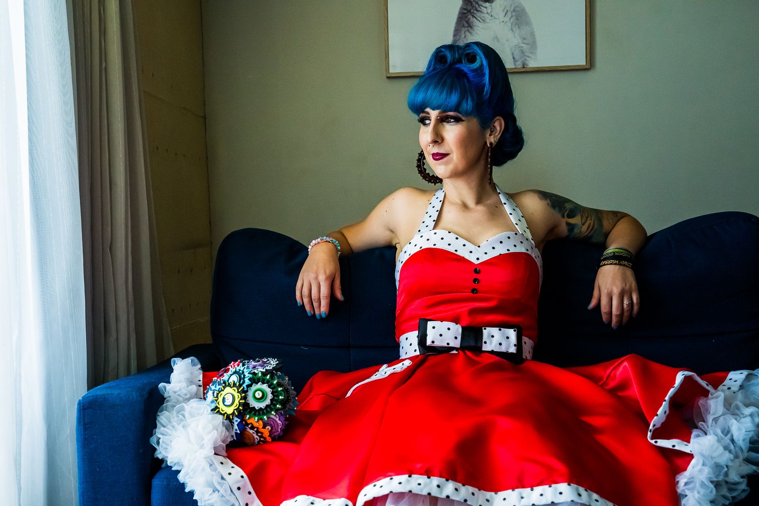A person in a vibrant red vintage-style dress with white trim reclines on a blue sofa near a window.