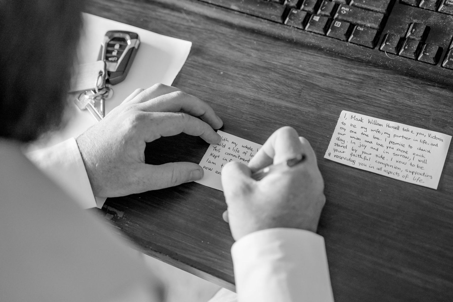 Black and white photo of someone writing in a notebook at a wooden desk.