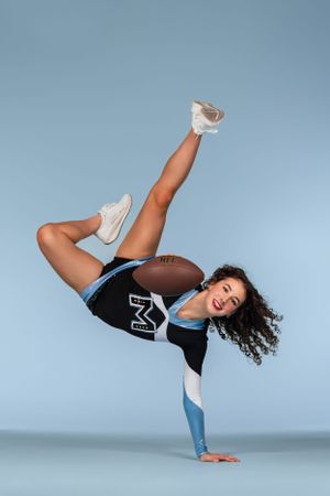 Athletic high school dancer in black and blue activewear performs dynamic breakdance freeze move against light blue background.