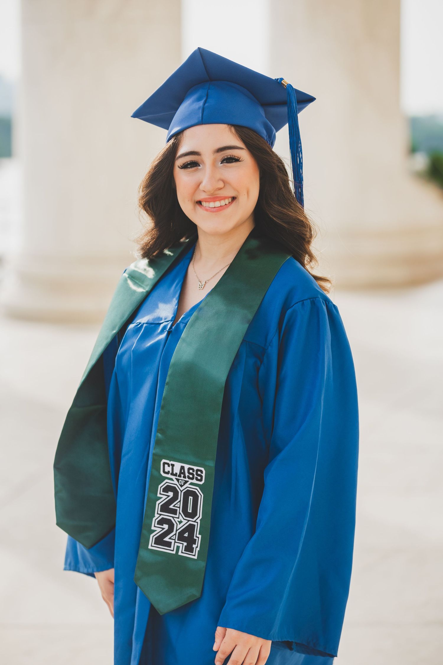 Graduate wearing blue cap and gown with green sash displaying Class of 2024.
