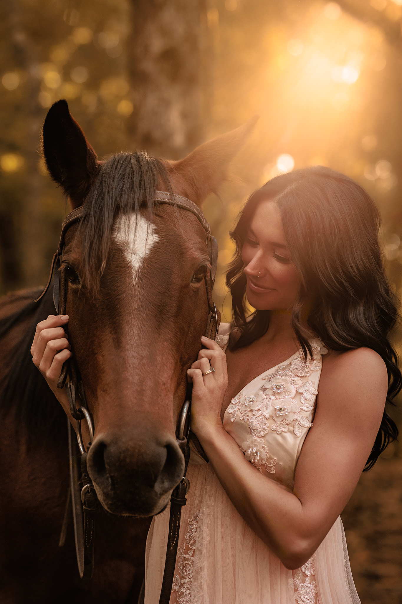 A brown horse and person in a lace dress share a tender moment at sunset with golden bokeh lighting in the background.