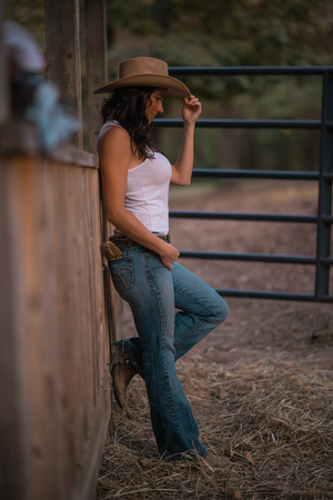 Country western style with cowboy hat and jeans leaning against rustic fence at sunset in casual ranch setting.