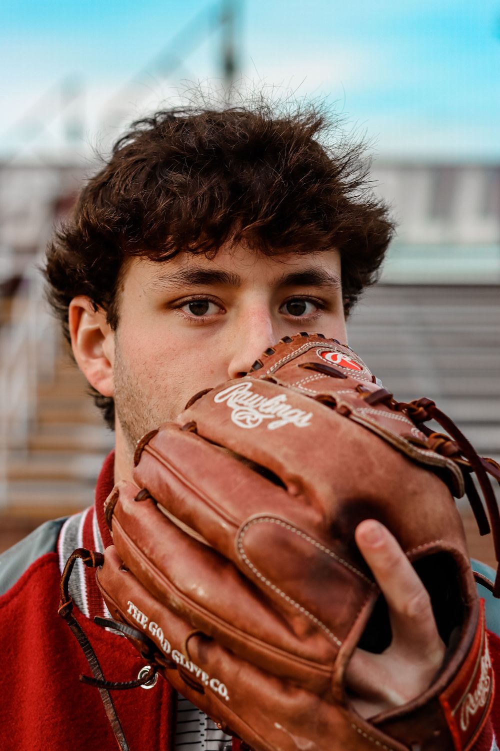 Baseball player in red shirt poses with leather baseball glove close to face.