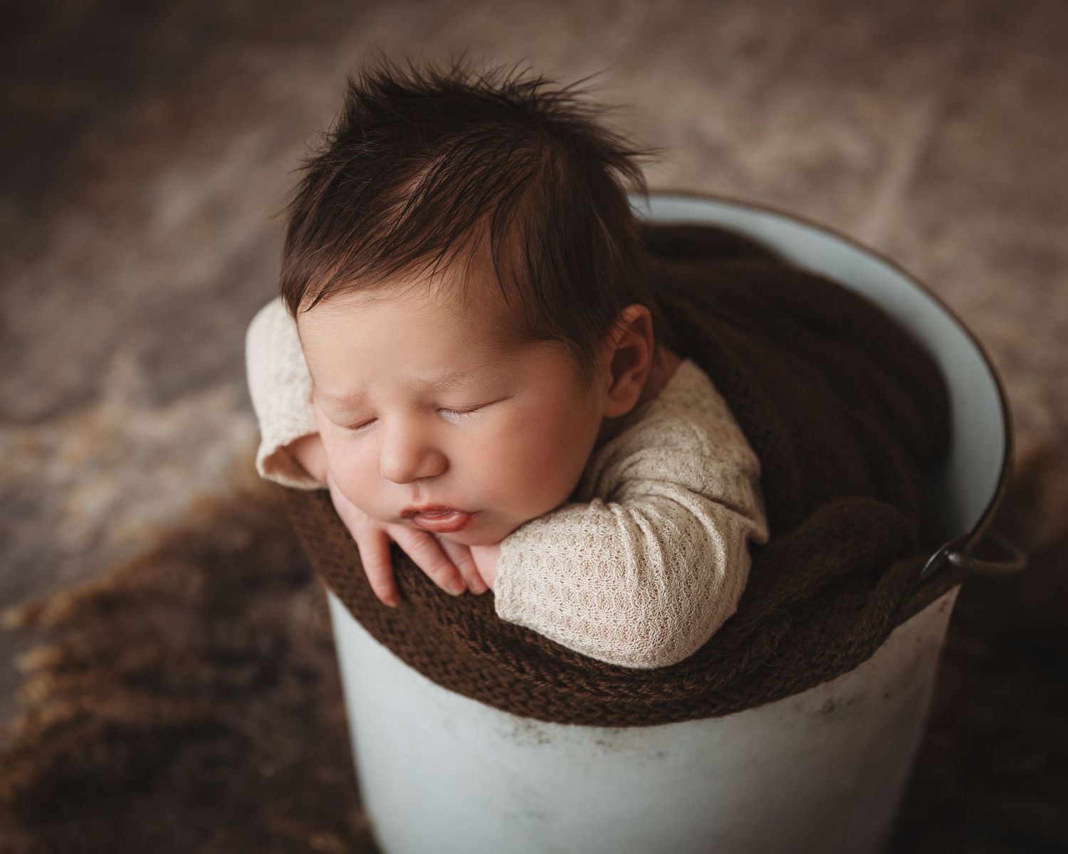 Artistic newborn portrait in rustic metal container with dark brown textured backdrop.