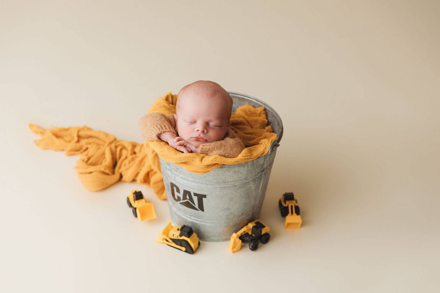 Sleeping newborn in yellow wrap posed in vintage metal bucket prop.