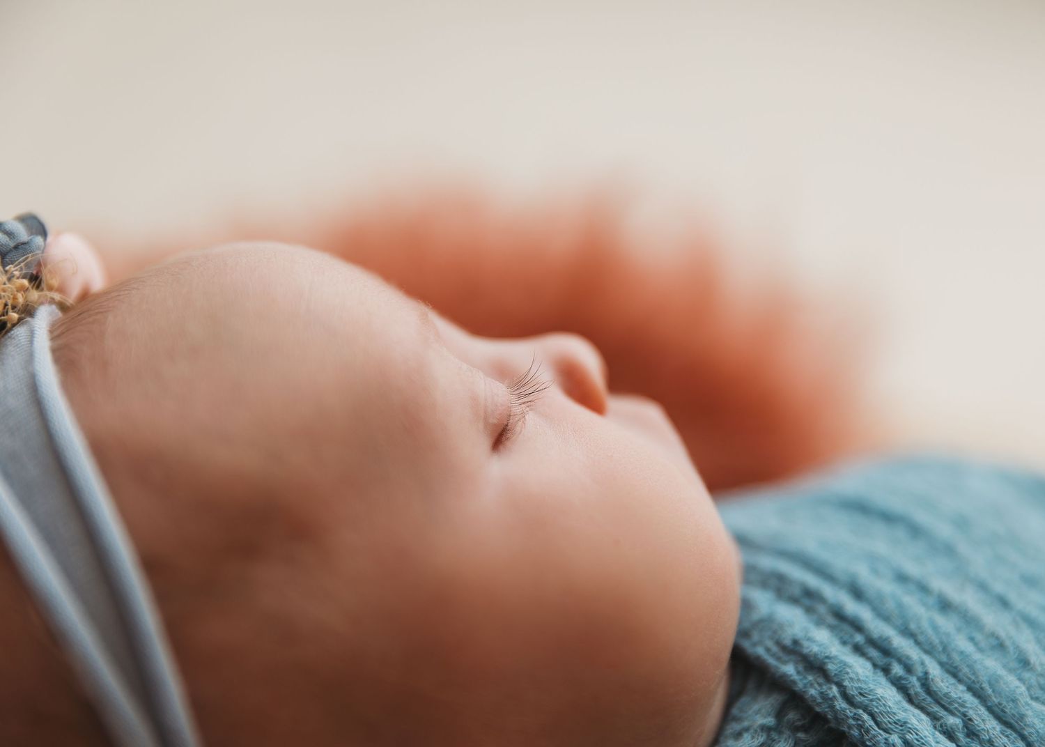 Close-up profile view of sleeping newborn on soft teal blanket.