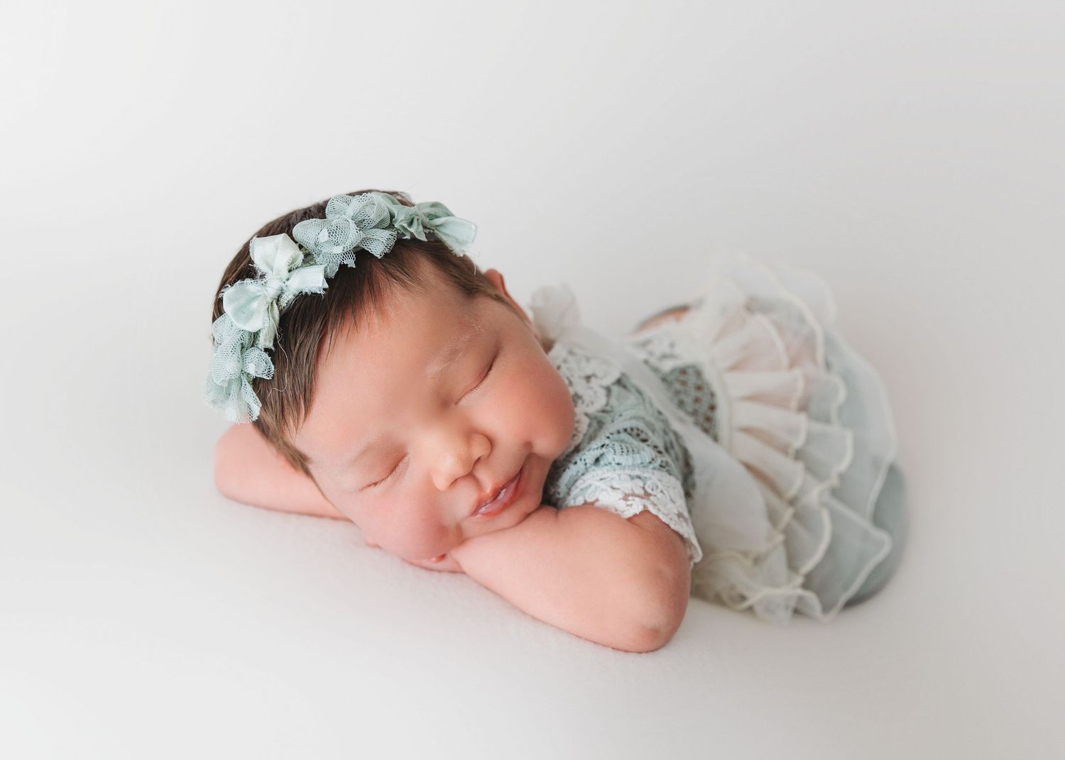 Newborn in mint green outfit with floral headband sleeping during professional photoshoot.