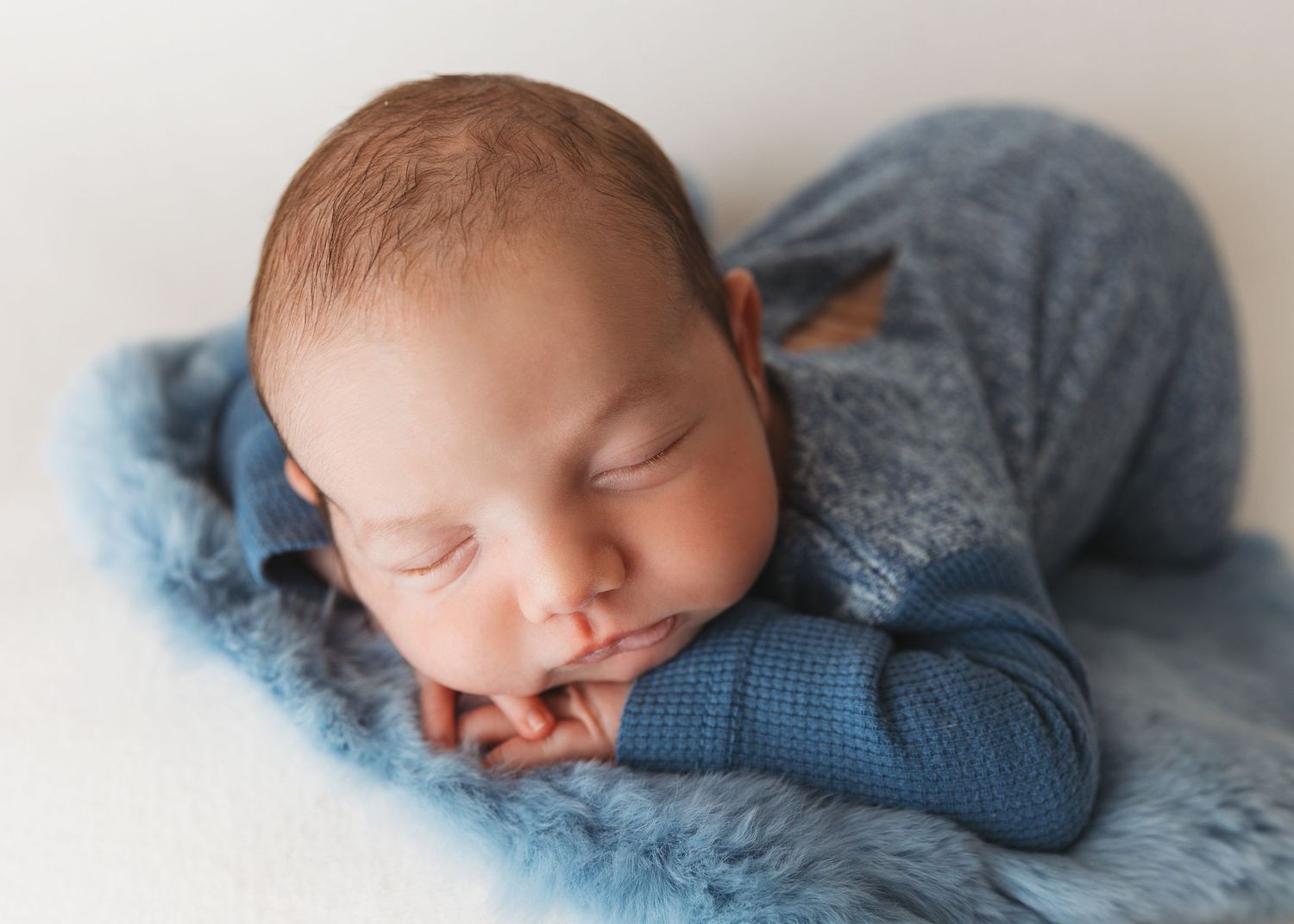 Sleeping newborn wrapped in cozy blue knit blanket during professional photo session.
