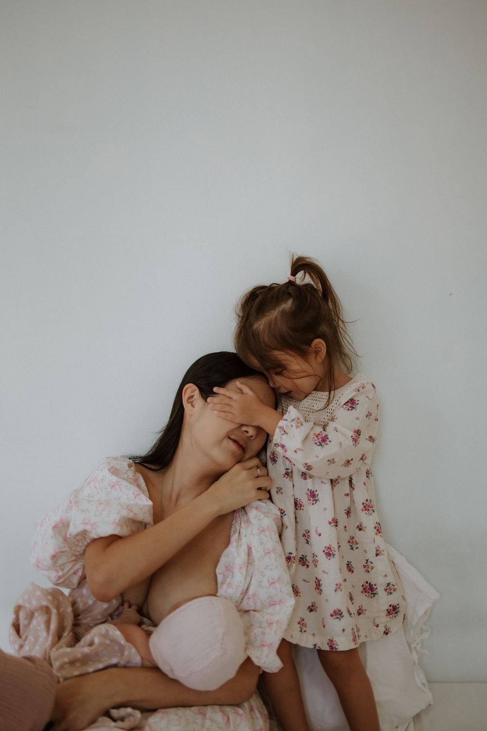Tender moment captured against white wall showing maternal affection.