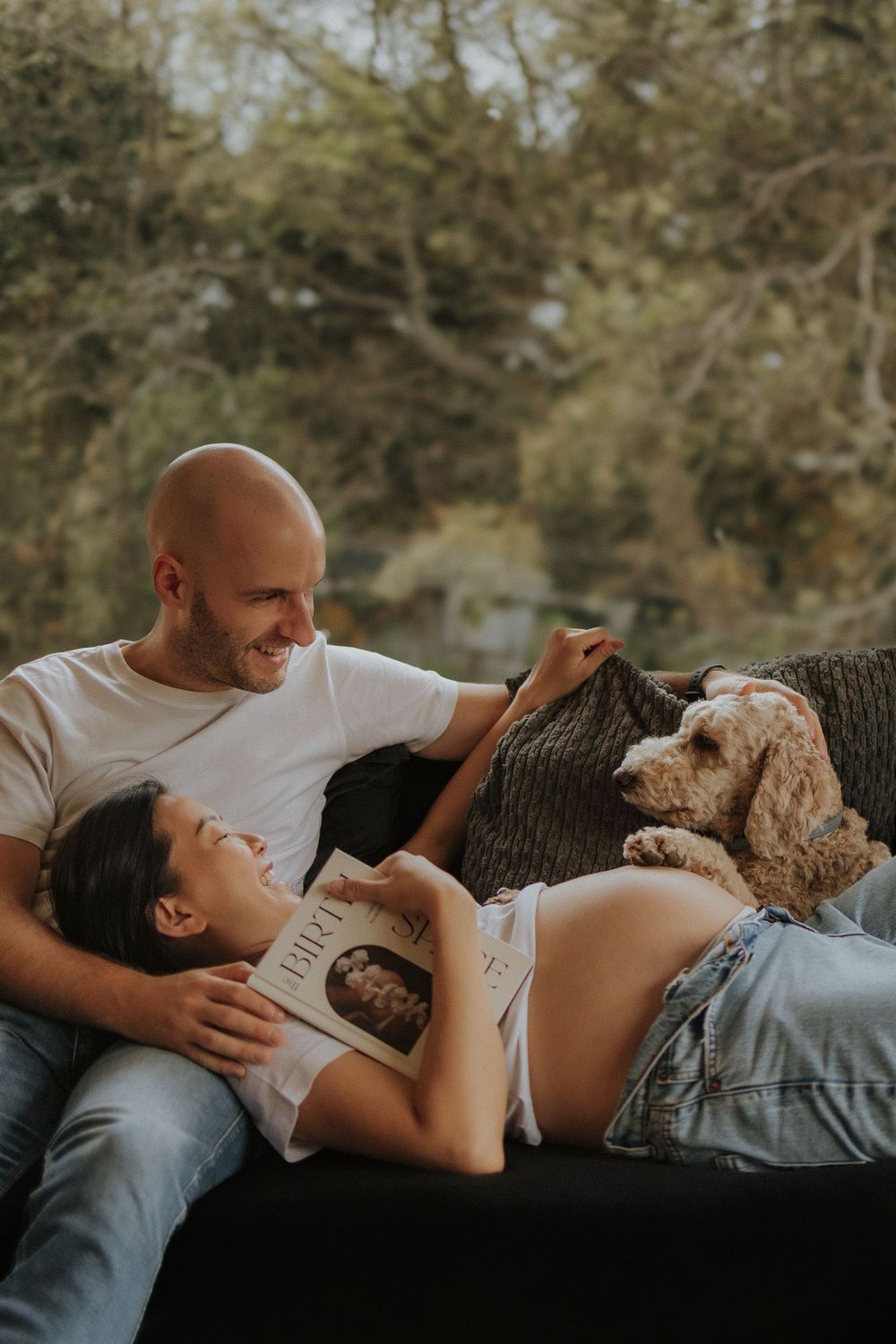 Couple relaxes outdoors with their furry companion, a Goldendoodle dog, during a tender maternity photo session.