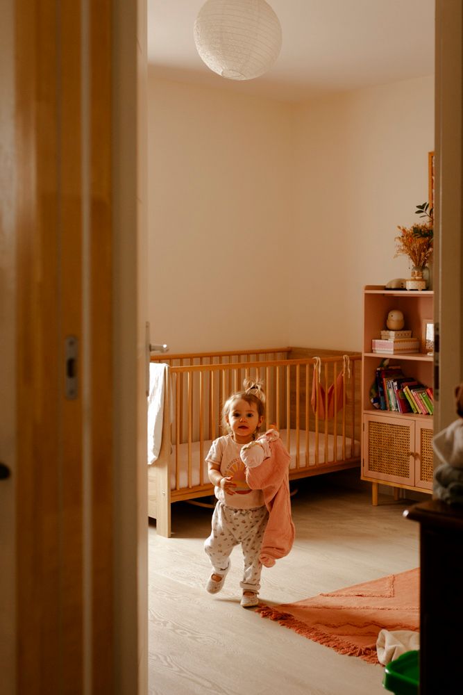 Petite fille dans sa chambre pendant un shooting photo de famille, avec rayon de lumière qui entre par la fenêtre.