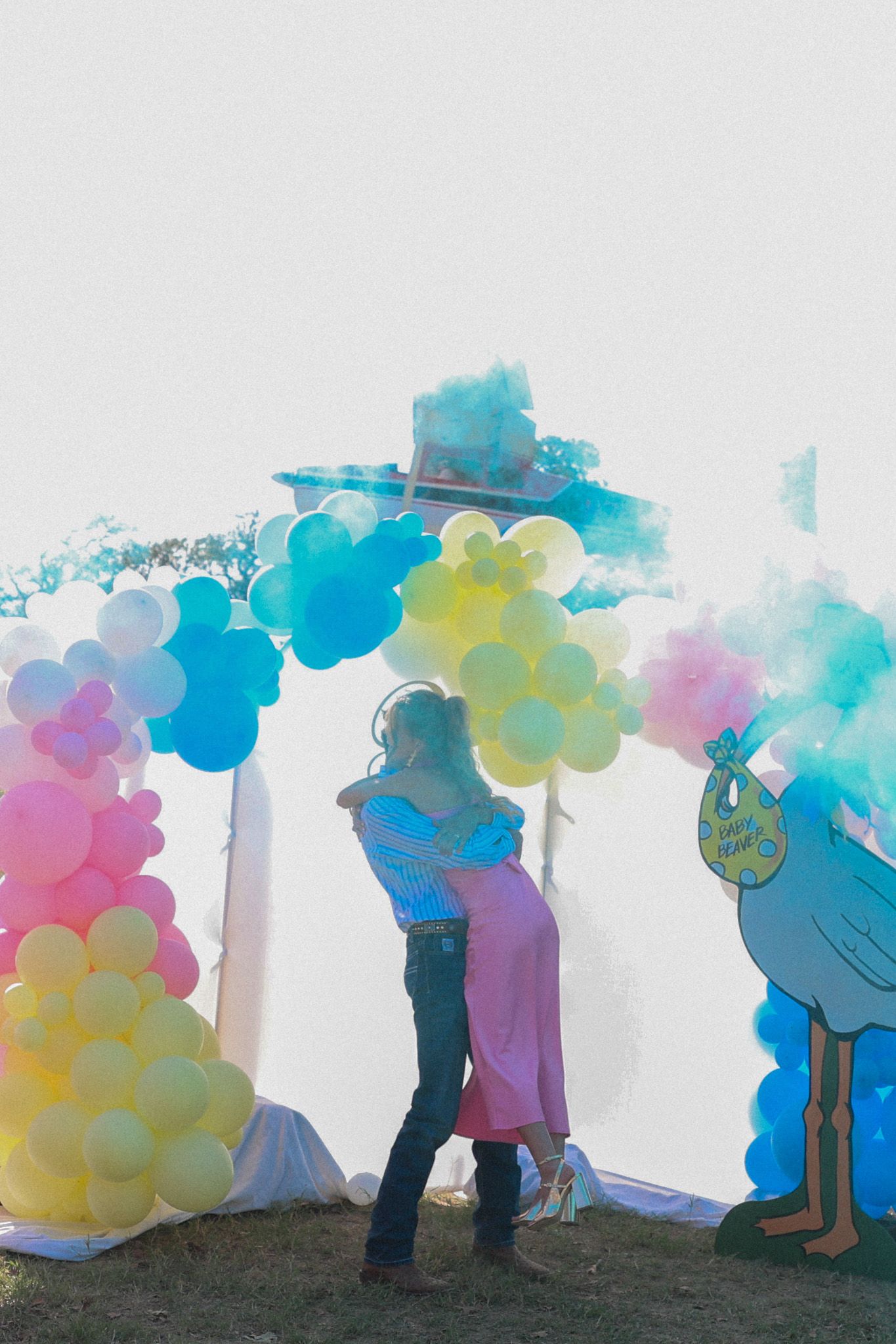A colorful balloon arch installation with rainbow hues stands against a light background as silhouettes interact beneath it.