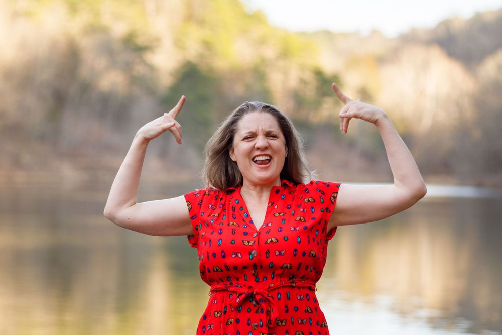 Woman in red dress expressing joy and celebration outdoors by a lake.
