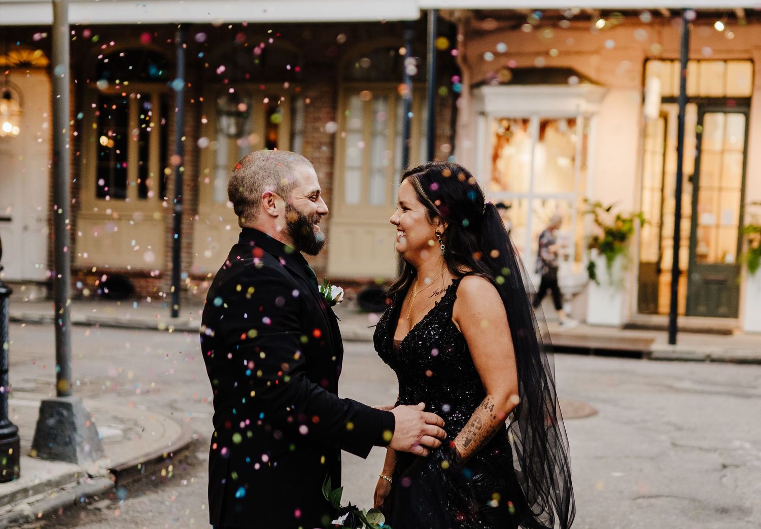 A romantic couple shares a joyful moment on a city street while confetti falls around them in golden light.