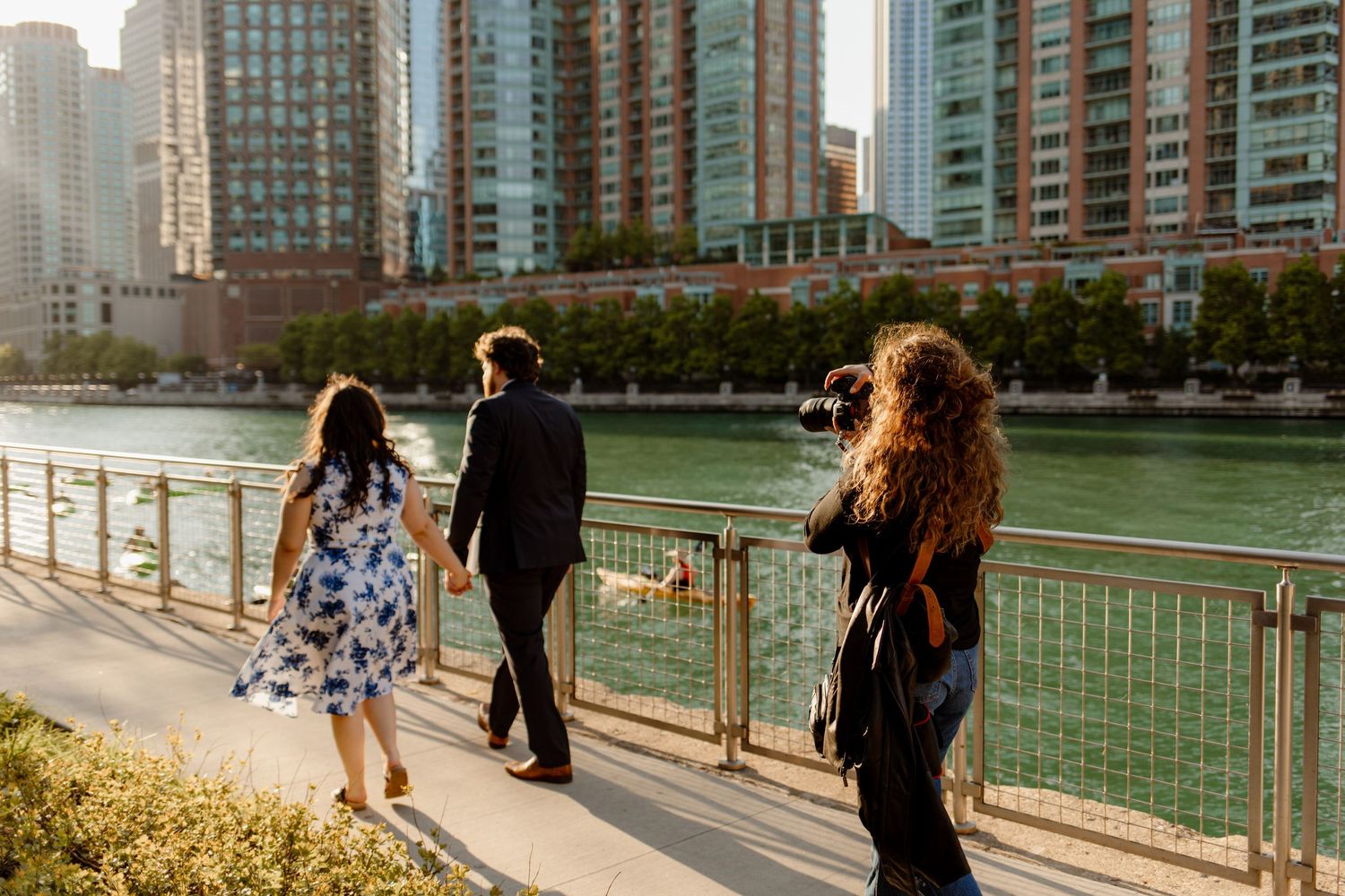 Group walking along a waterfront path with modern city buildings in background.