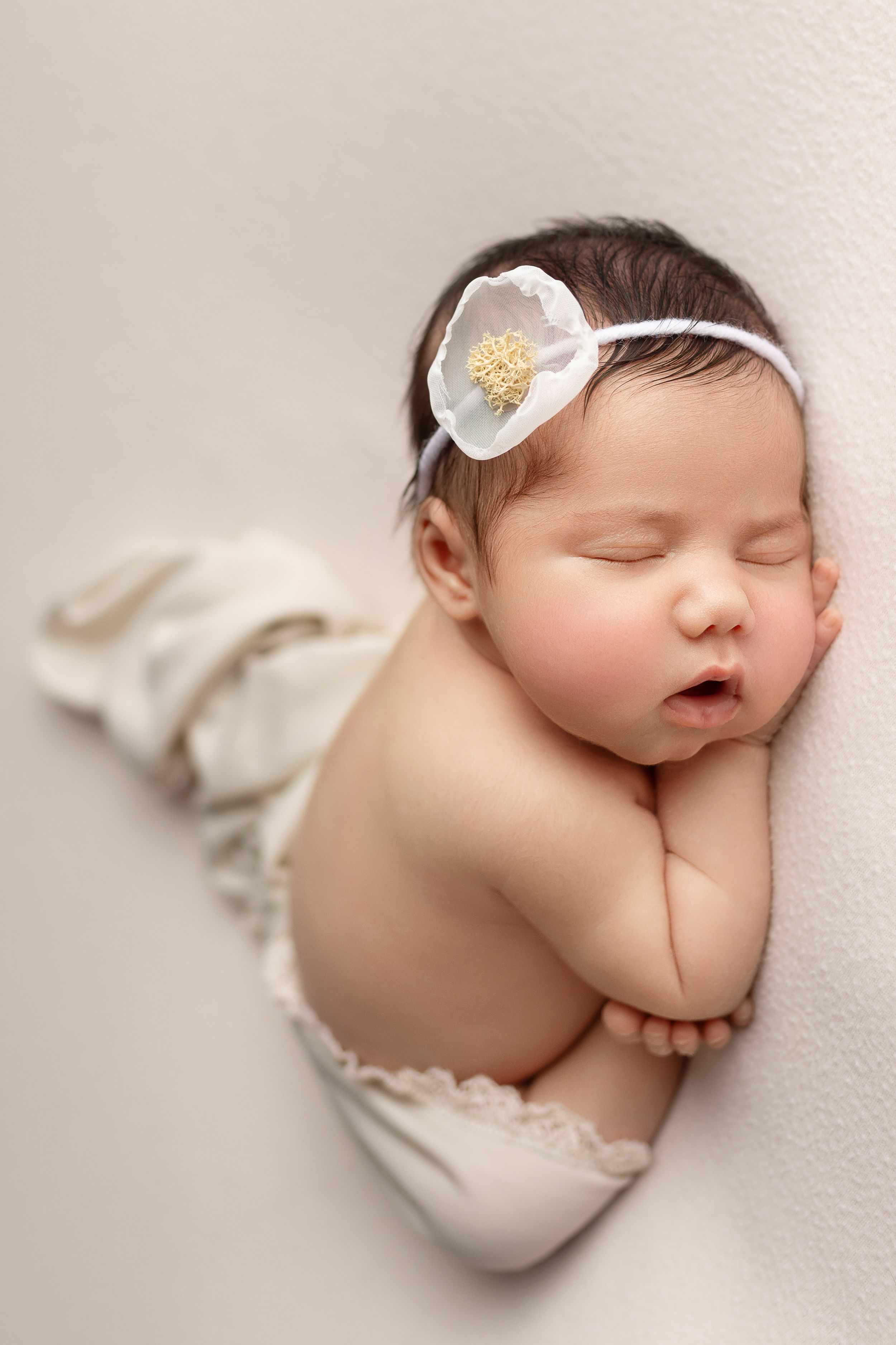newborn baby girl asleep in taco pose with white simple flowered headband, captured by cedar park newborn photographer