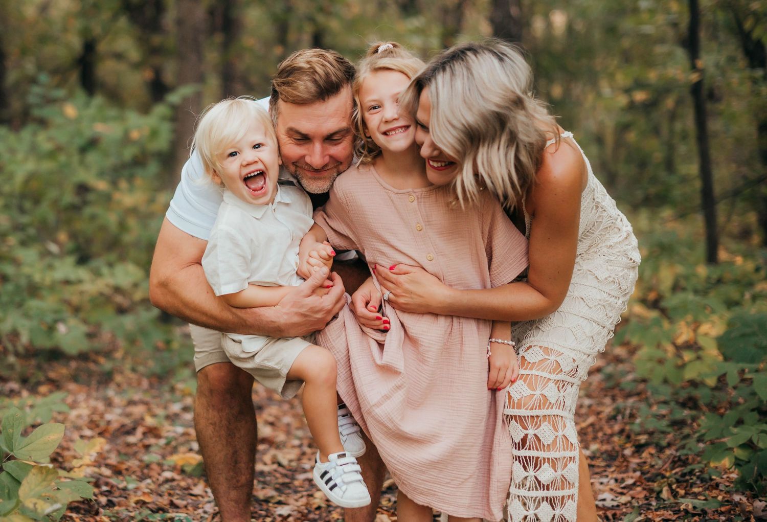A family shares a joyful moment together while standing in a forest setting during autumn.