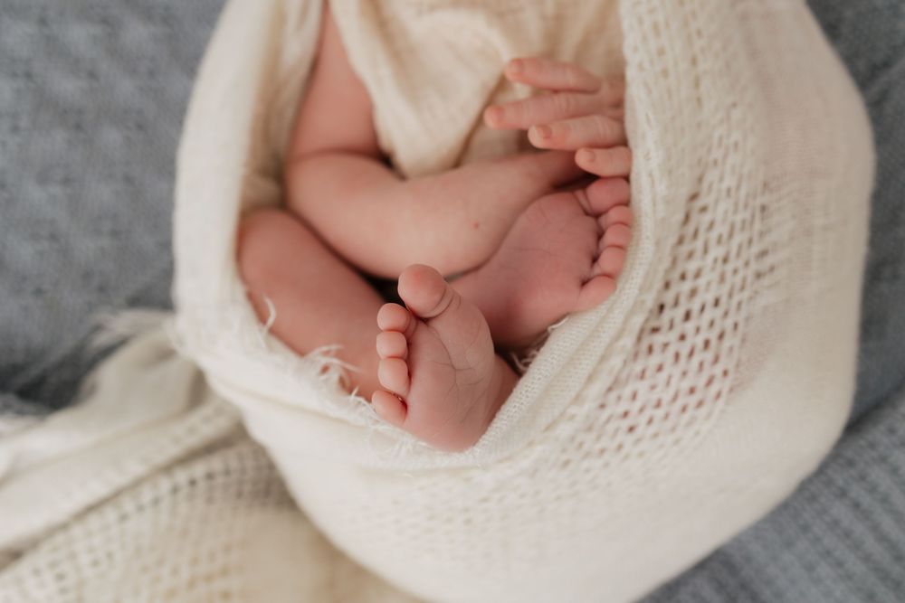 Close-up of a newborn baby's tiny feet and hands wrapped in a soft cream knit blanket.