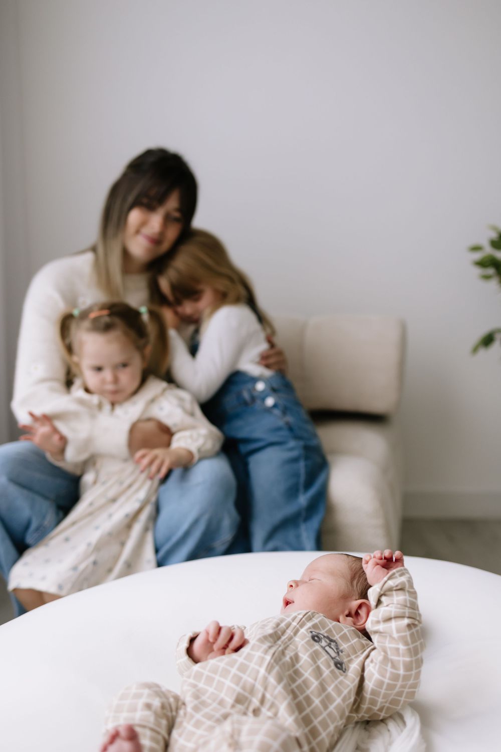A mother sits with two young girls on a chair while a newborn baby lies in the foreground.