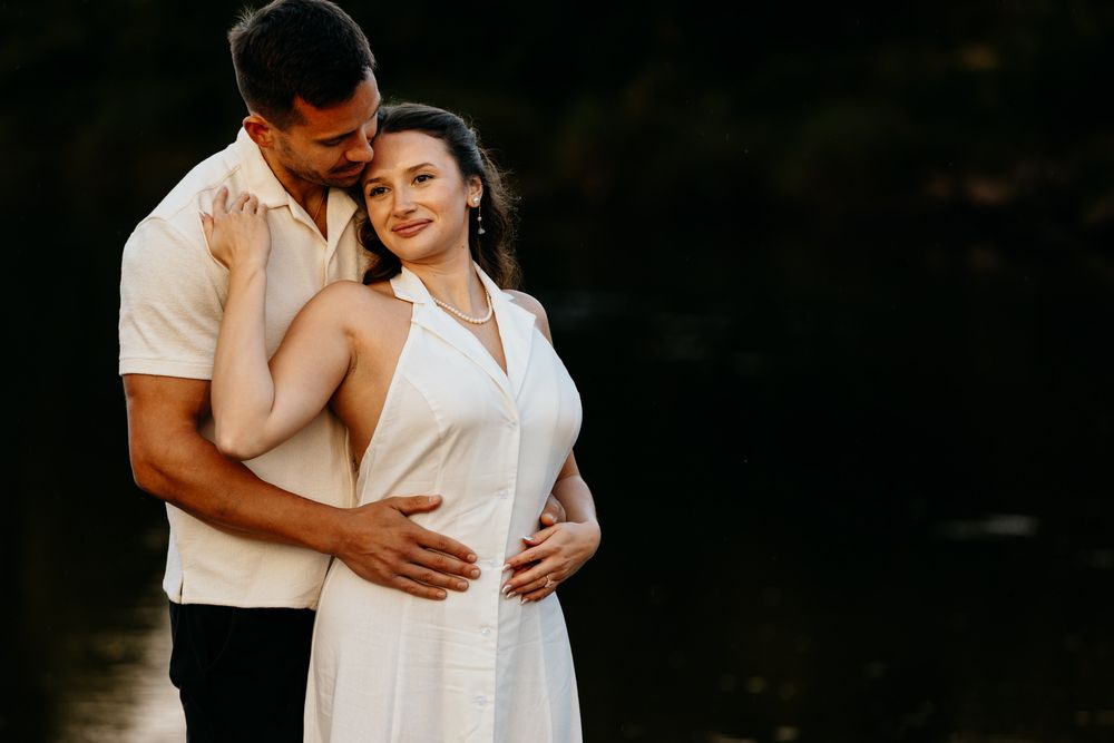 Romantic couple embrace while wearing white outfits outdoors.