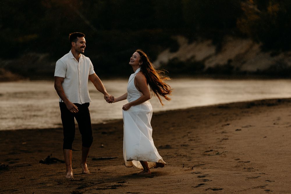Couple walking along a sandy beach at sunset.