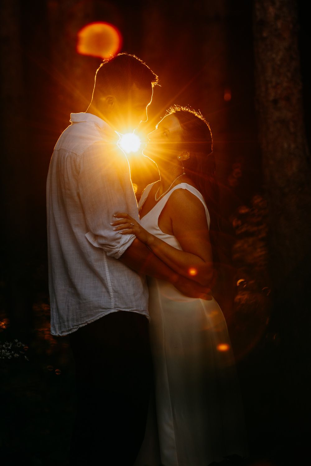 Silhouette of a couple embracing during sunset with dramatic lens flare.