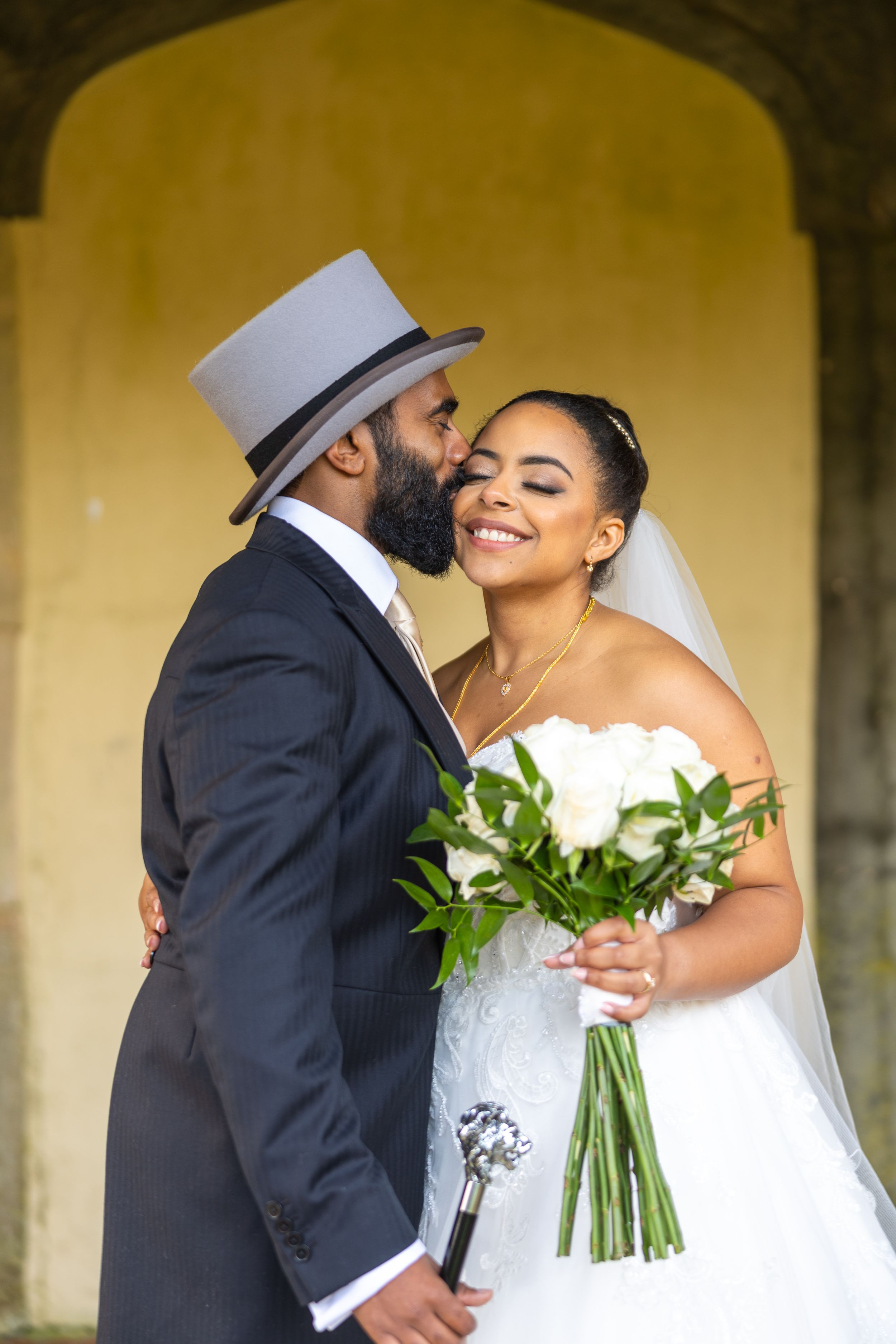 A tender wedding moment captured under a stone archway with a beautiful white bouquet of flowers.