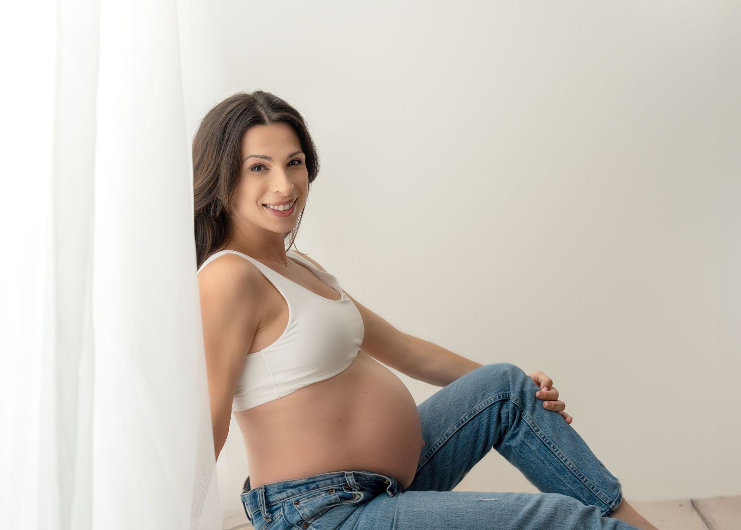 Silhouette of pregnant woman in side profile against white backlit curtains.