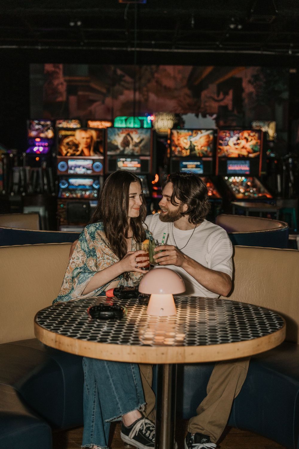 A couple shares an intimate moment at a dimly lit restaurant table with patterned surface and drinks.
