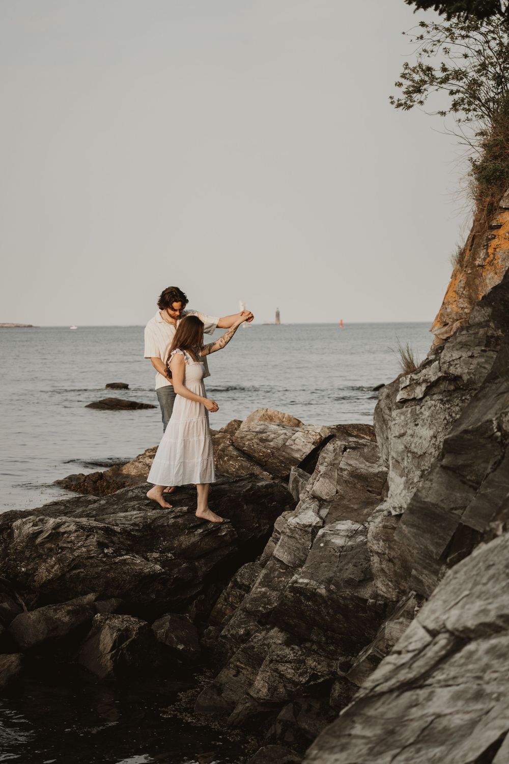 A couple dances together on rocky coastal cliffs overlooking the misty ocean.
