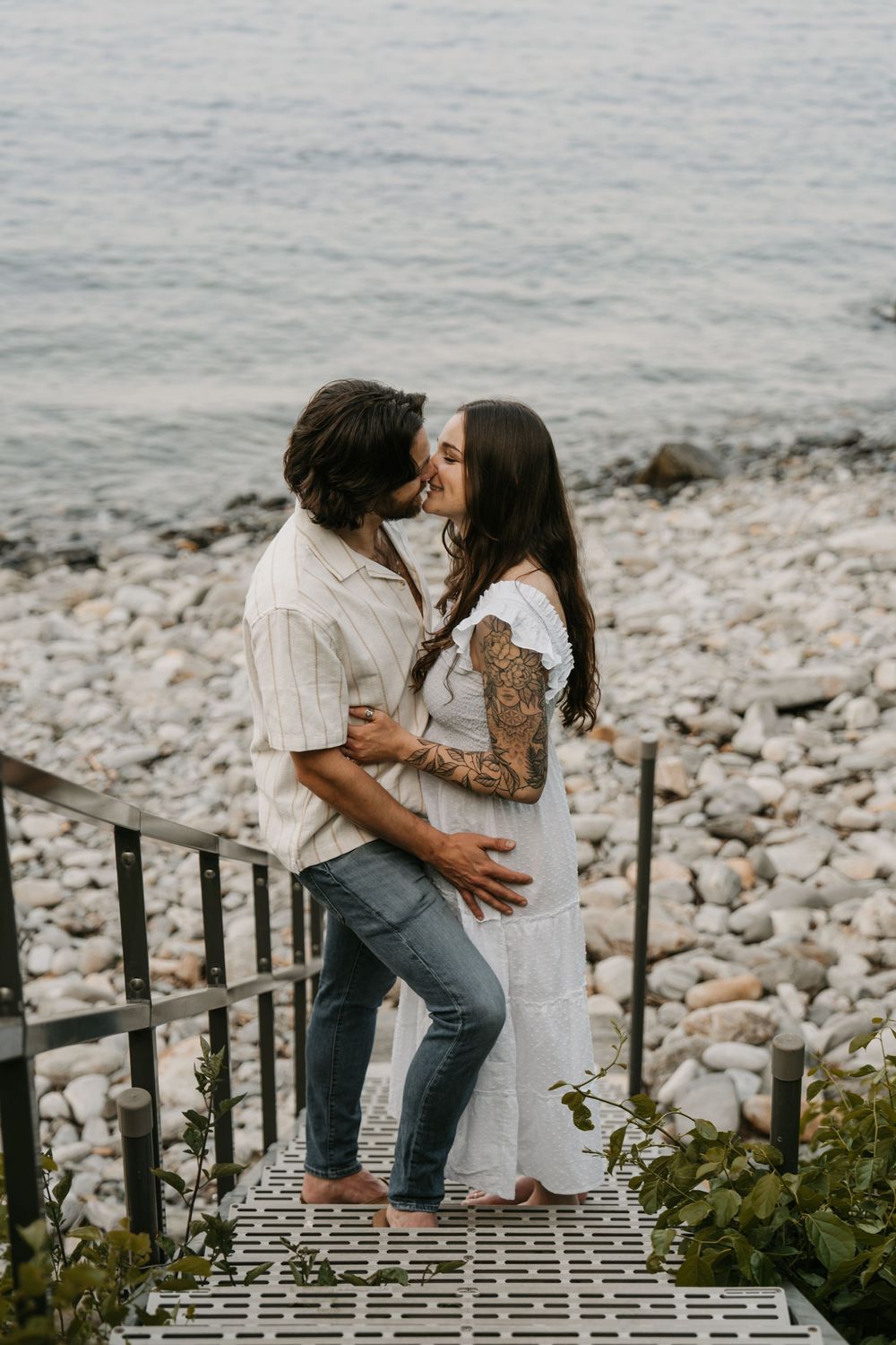 A romantic couple shares intimate moments on rustic wooden stairs overlooking a rocky beach and ocean.