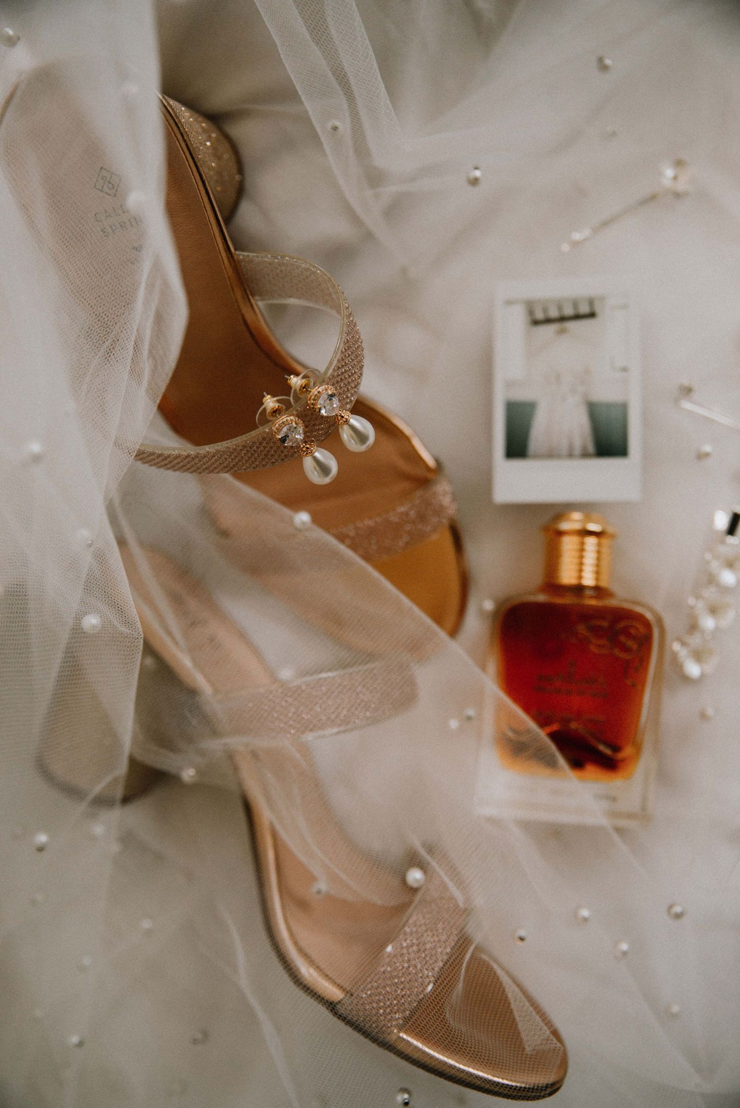 Detail flat lay of a bride’s wedding shoes, perfume, and an Instax photo of her dress, capturing elegant bridal details
