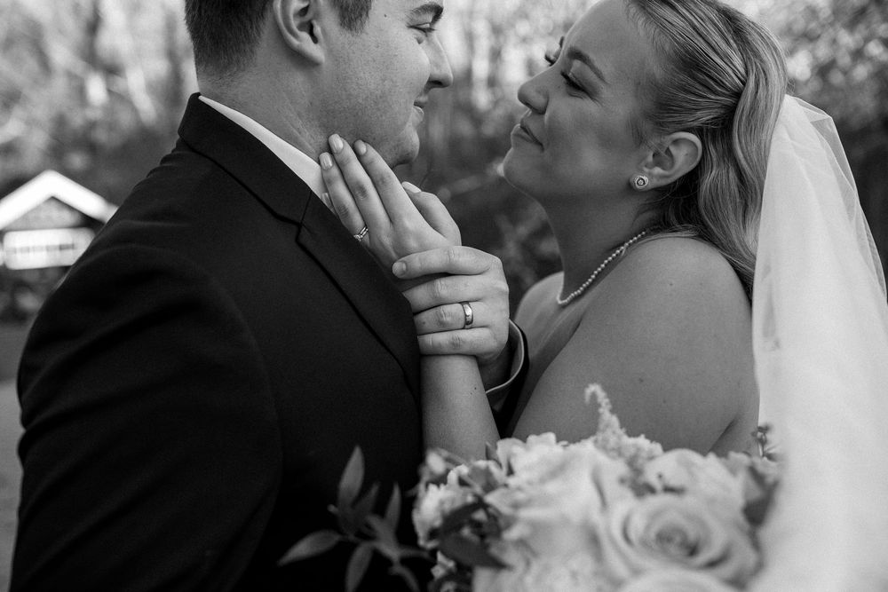Black and white wedding photo of bride and groom sharing an intimate moment, bride holding bouquet of roses.