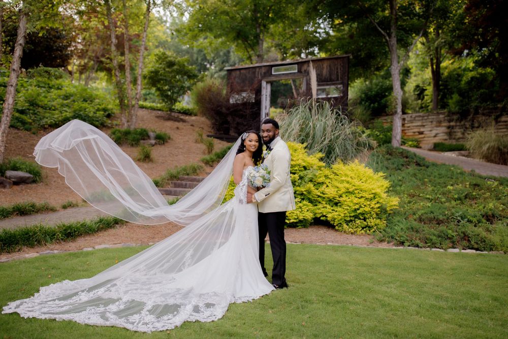 A dramatic wedding photo with a flowing cathedral veil in a lush garden setting.