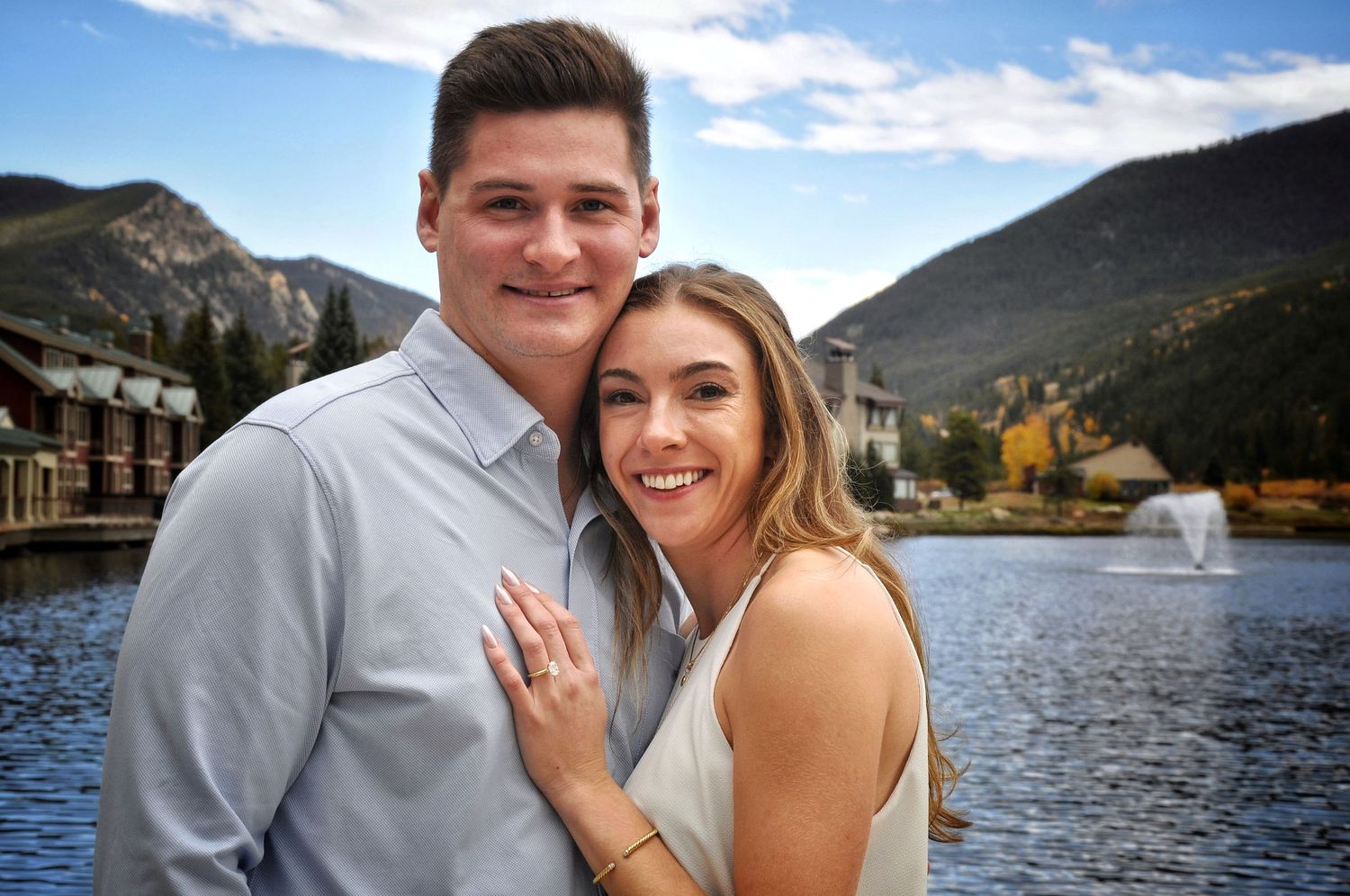 Man embraces his new fiancee with a lake and mountains in the background