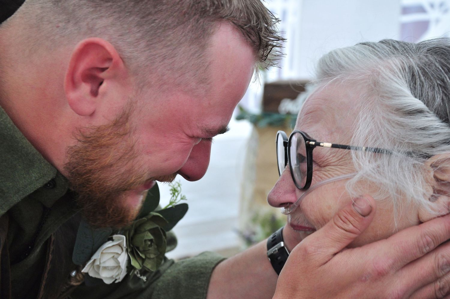 Young man clutching the face of his grandma in his hands before he gives her a kiss.