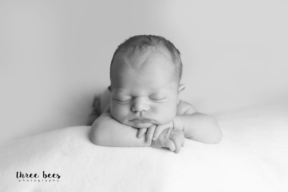 Black and white portrait of peaceful sleeping newborn baby resting head on folded arms.
