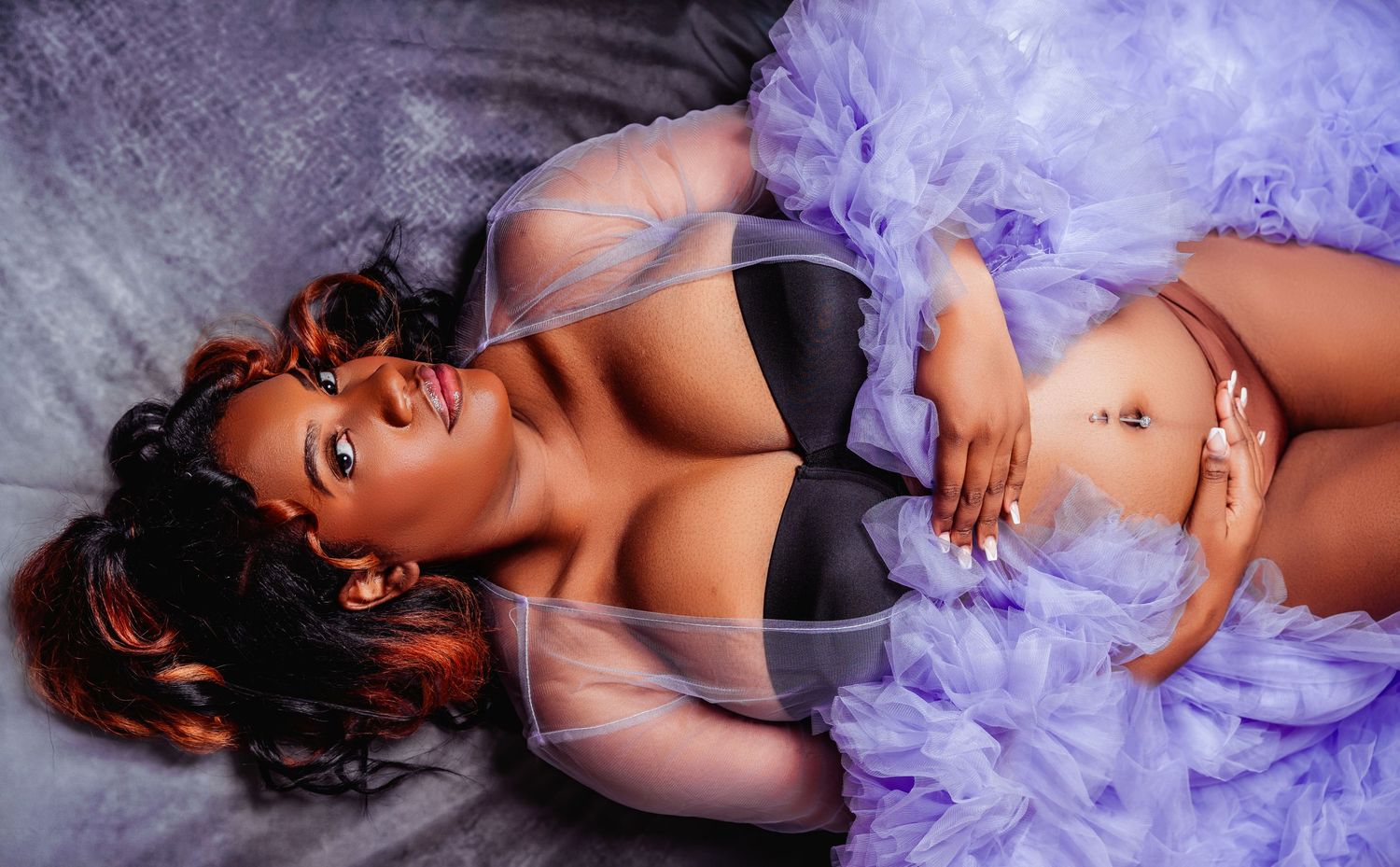 A boudoir photoshoot featuring lavender tulle fabric and black lingerie in a dramatic pose against grey backdrop.