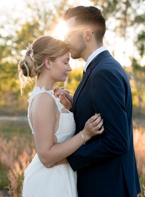Bride and groom share a romantic golden hour moment outdoors, with sun flare glowing behind them.