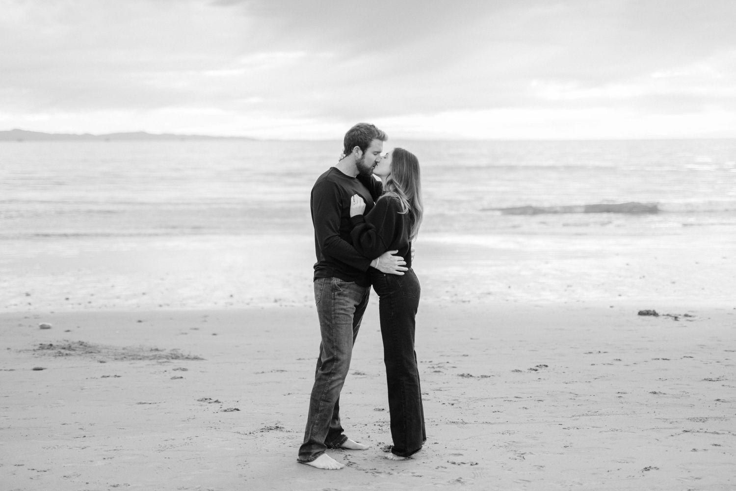 Black and white beach wedding photos showing couple embracing by the ocean.