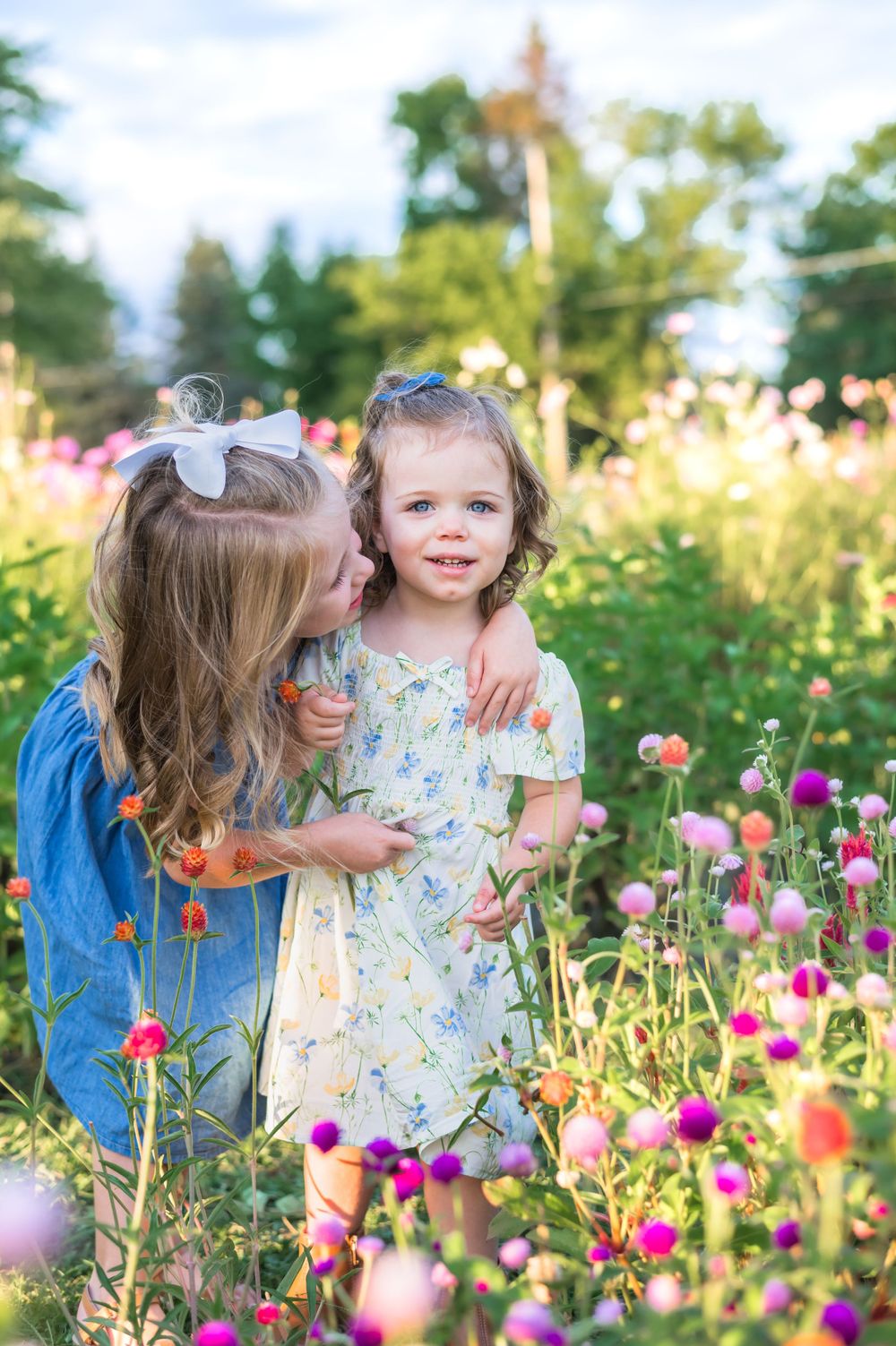 Two kids share a sweet moment among vibrant pink and purple wildflowers in a summer garden.