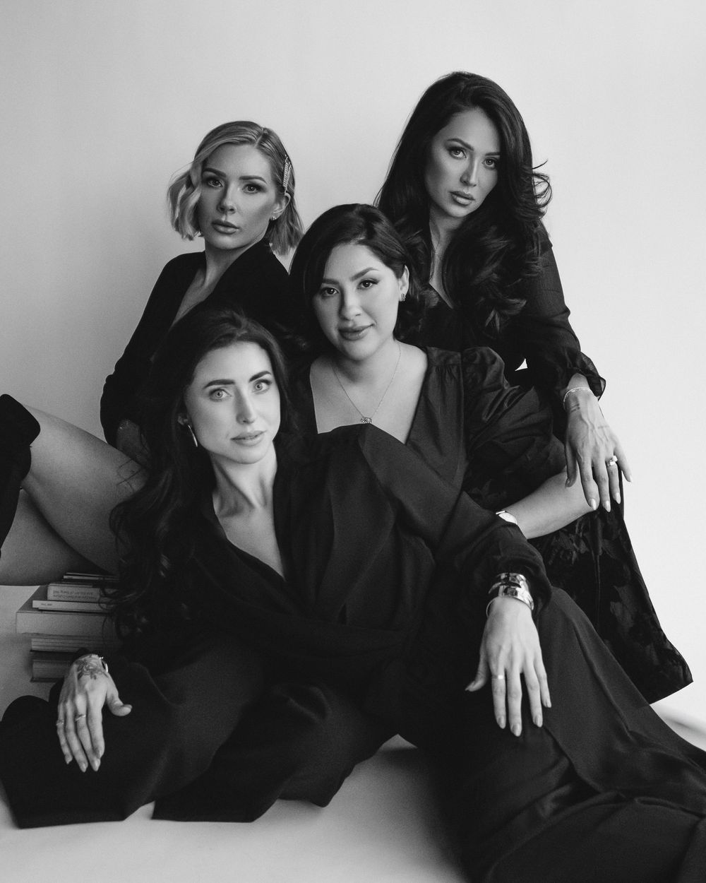 A black and white portrait of four women in dark clothing posing elegantly together on a couch.
