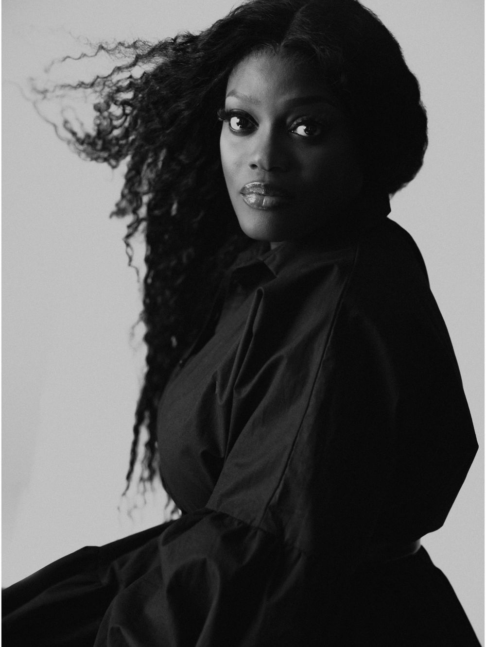 Black and white portrait featuring flowing natural hair and dark clothing against light background.