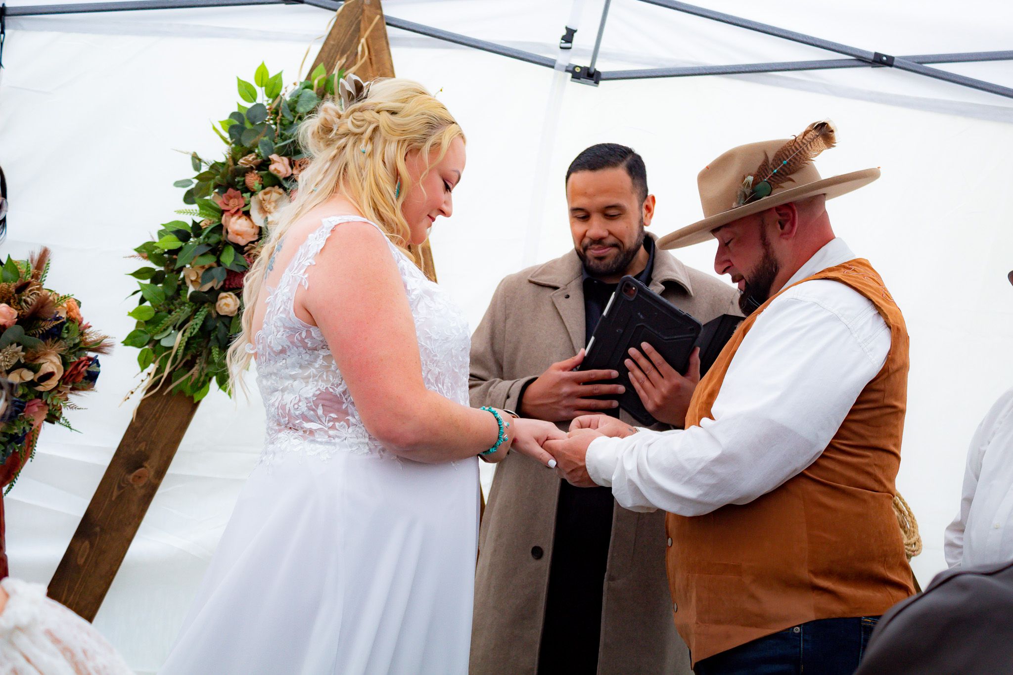 Wedding ceremony under white tent with wooden cross and floral decorations.