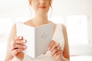 Hands holding a white wedding vow book or ceremony program in soft natural light.