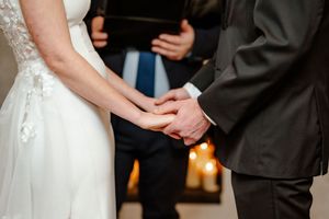 Formal wedding ceremony detail showing hands and formal attire during exchange of vows.