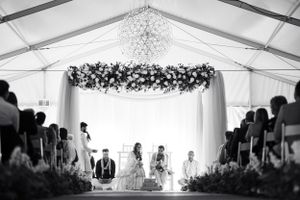 Wedding reception tent interior with elegant chandelier and floral ceiling installations.