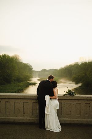 Silhouetted couple embracing on stone bridge at misty sunset.